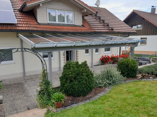 Vordach Vorderansicht eines Hauses mit Überdachung, Garten und blühenden Pflanzen.