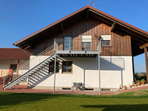Eisentreppe Zweigeschossiges Haus mit Holzverkleidung, Treppe und Rasenfläche im Vordergrund.