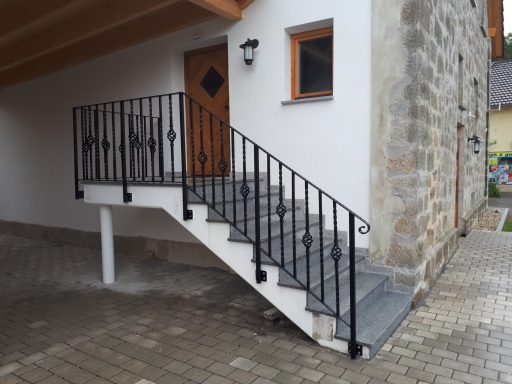 Treppengeländer Eingangstreppe mit grau gepflasterten Stufen und schwarzer Metallgeländer.