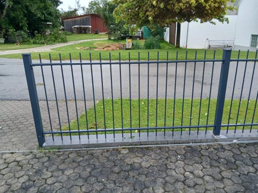 Zaun Graue Metallzaun mit senkrechten Streben, angrenzend an einen grünen Rasen.