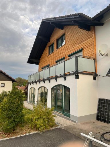 Balkongeländer Mehrstöckiges Haus mit Holzverkleidung, Balkon und großen Fenstern.