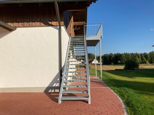 Eisentreppe Metallene Treppe an einem Gebäude, umgeben von Rasen und Bäumen unter blauem Himmel.