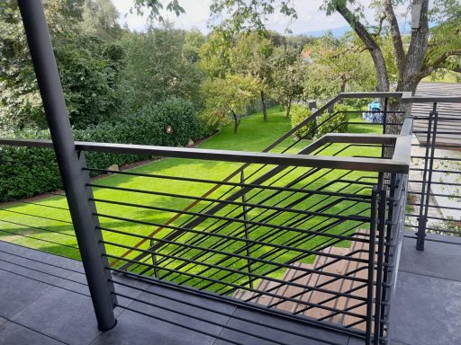 Geländer Blick von einem Balkon auf einen grünen Garten mit Bäumen und Rasenfläche.