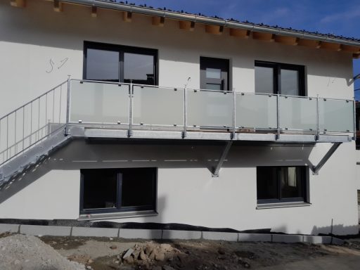 Balkongeländer Neues zweigeschossiges Gebäude mit Balkon und Glasgeländer, unter blauen Himmel.